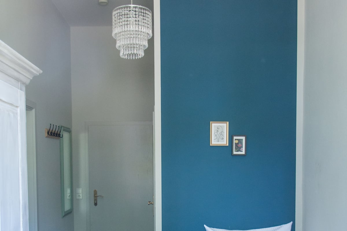 A bedroom with a bed, a blue chair, a chandelier, and a door.