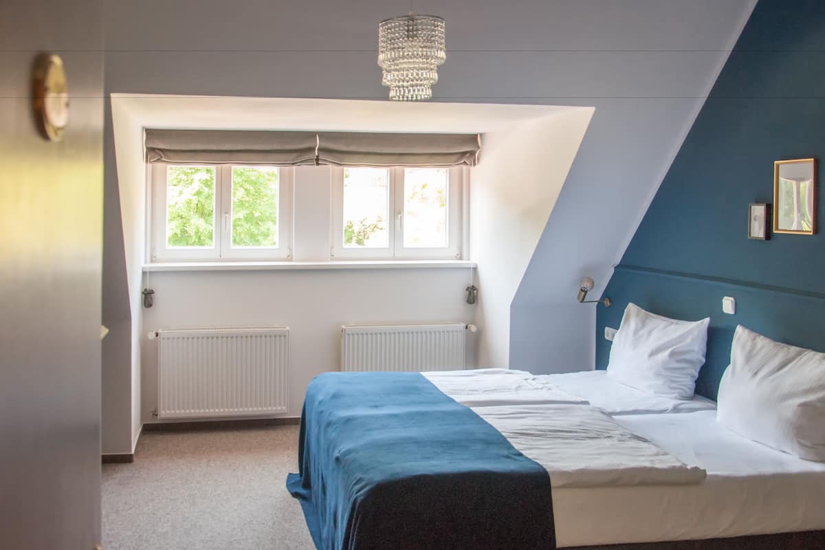 A bedroom with a bed, a window with curtains, a radiator, and a chandelier.