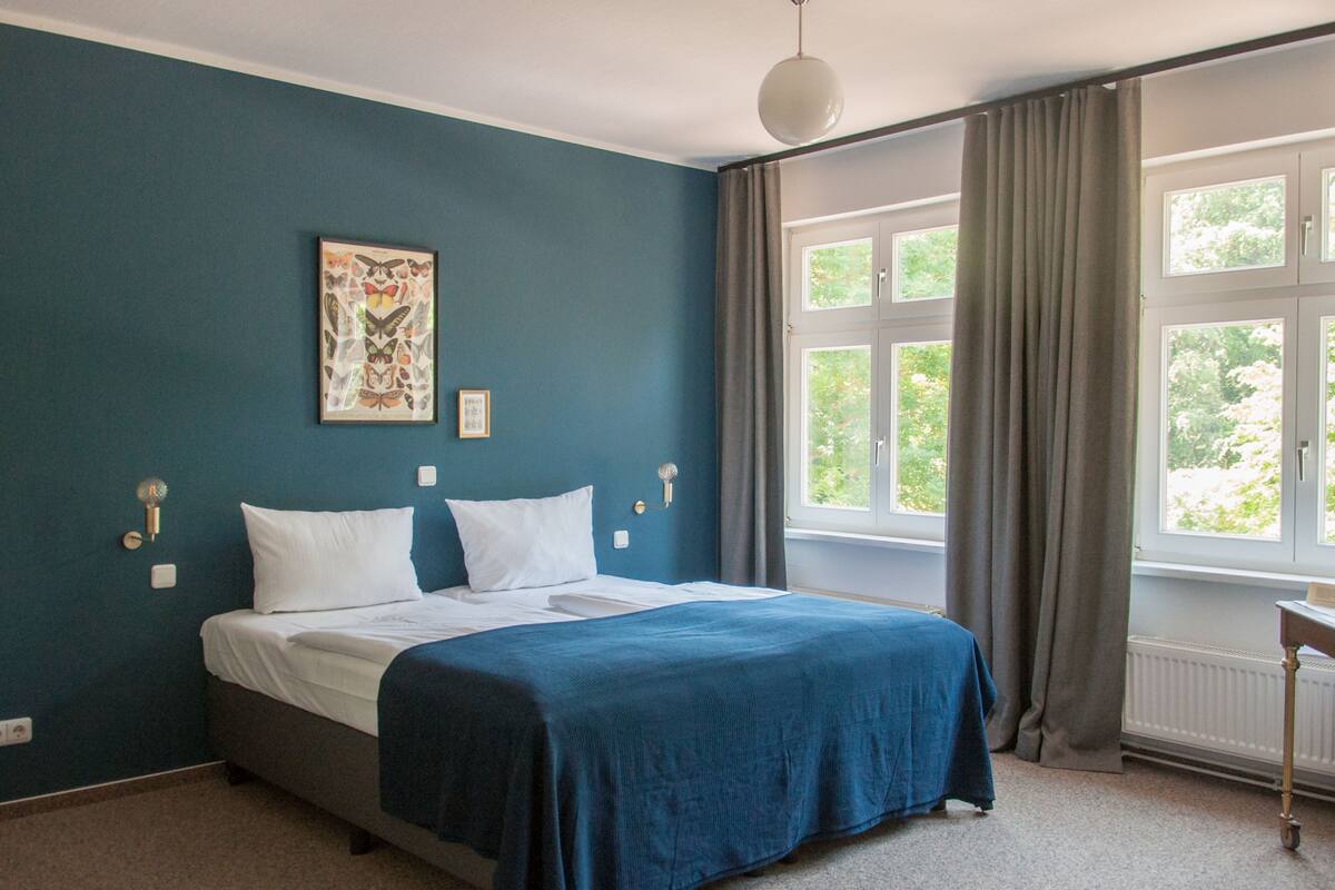 A bedroom with a bed, a window with curtains, and a wall-mounted light fixture.