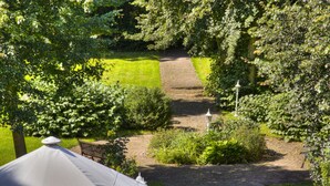 Un sendero de jardín con un banco, rodeado de abundante vegetación y una estructura de carpa blanca.