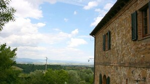 A stone building with green shutters, a grassy yard, and a view of distant hills.