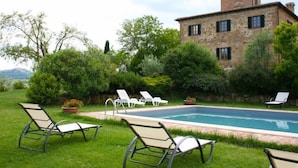 A stone building with a swimming pool, surrounded by lush greenery and white lounge chairs.