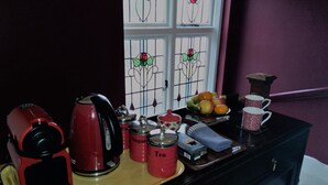 Una encimera de cocina con una cafetera, recipientes de azúcar y té, un frutero y dos tazas decoradas.