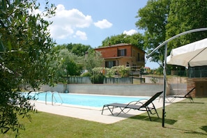 Una piscina con sillas de descanso, una casa de ladrillo al fondo y follaje circundante.