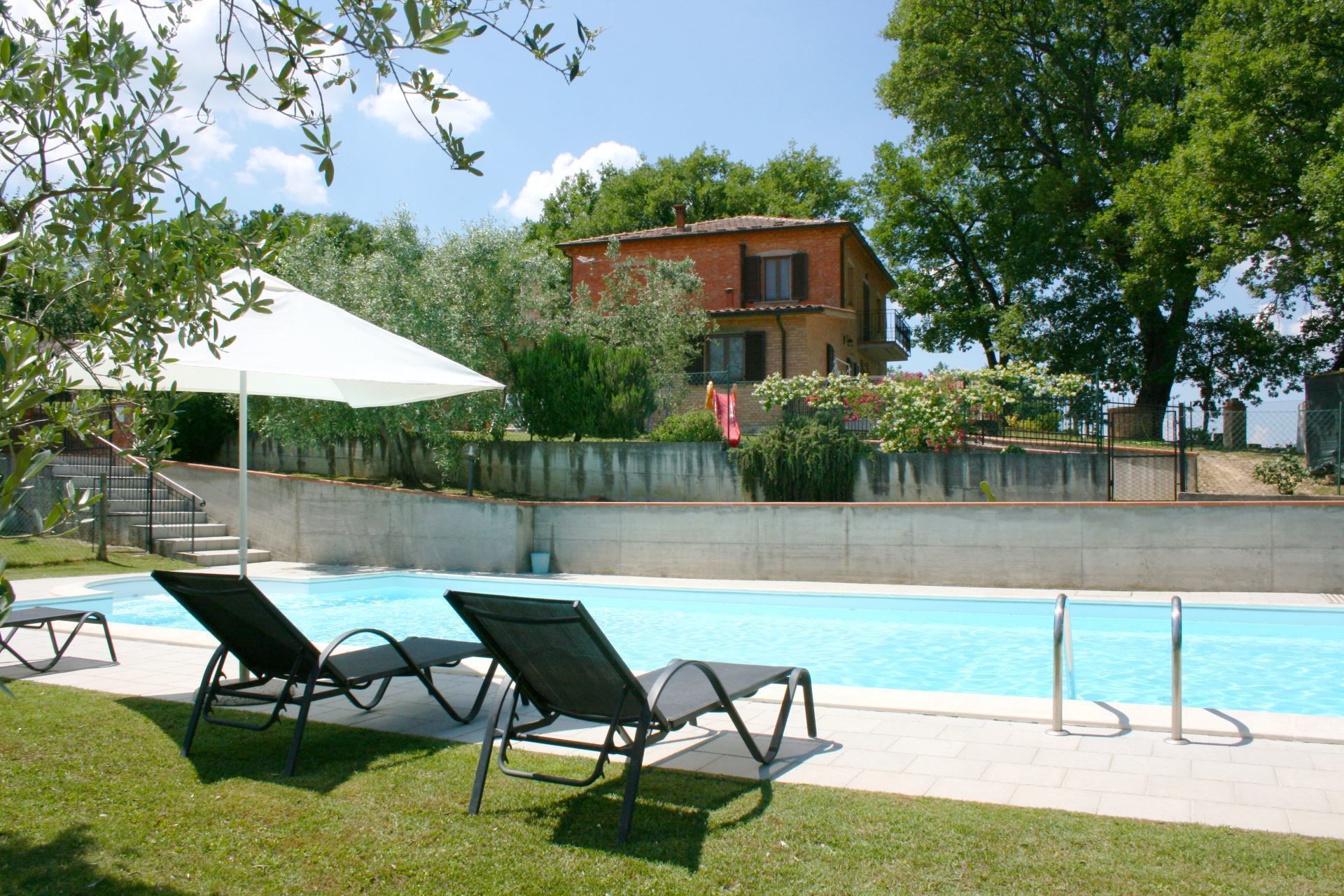 A swimming pool with lounge chairs, a white umbrella, and a house in the background.