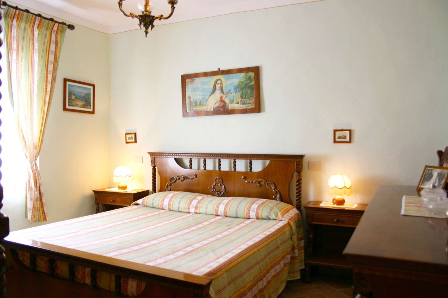 Un dormitorio con una cama de madera, dos mesitas de noche con lámparas, un cuadro en la pared y una cortina en la ventana.