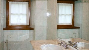 Ein Badezimmer mit Waschbecken, Spiegel, Fenster und gefliesten Wänden.