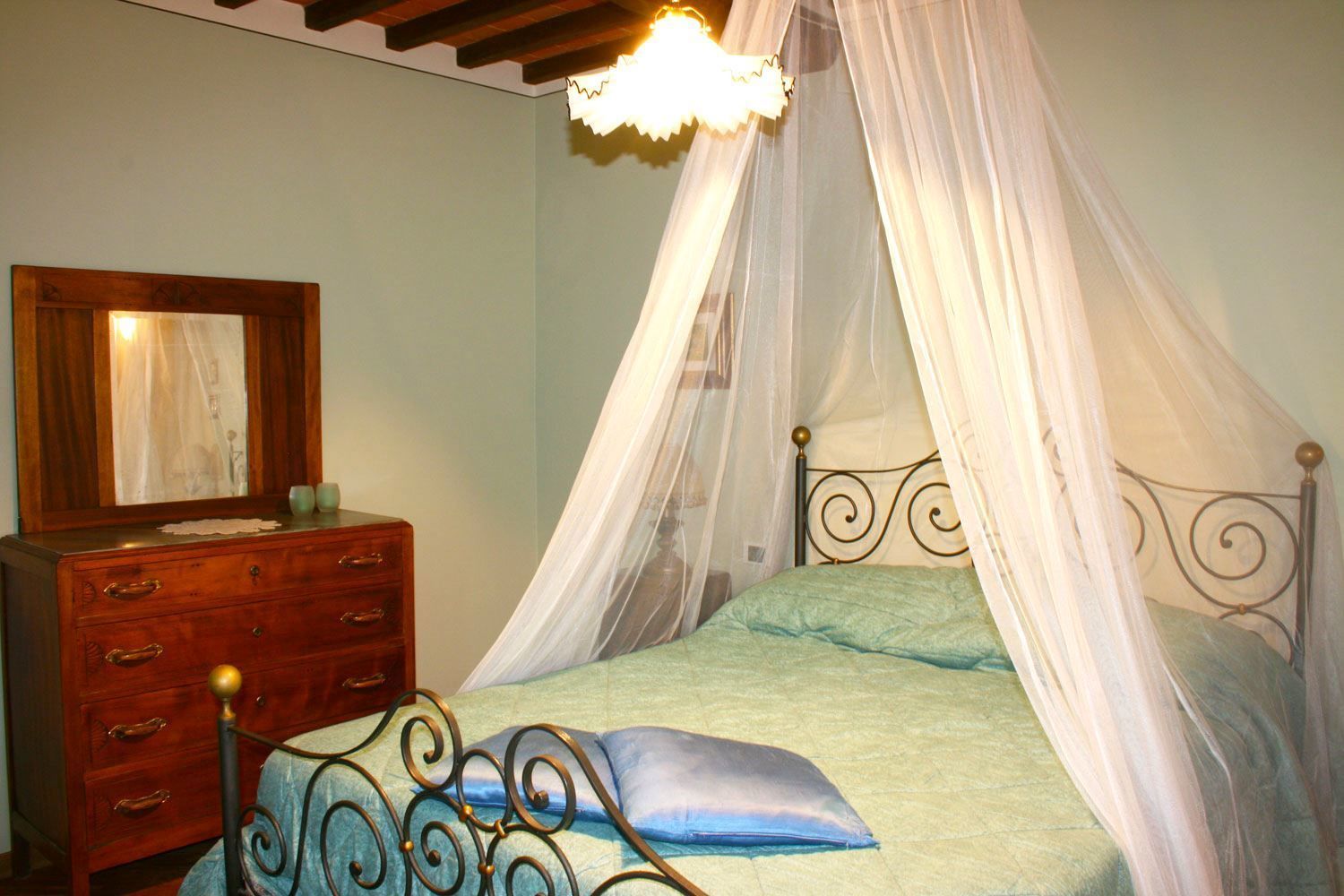 A bedroom with a canopy bed, a wooden dresser with drawers, and a mirror.