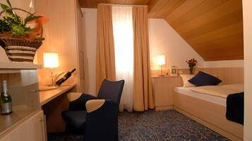 Et lille, hyggeligt værelse med seng, skrivebord med lampe, stol og et vindue med gardiner.