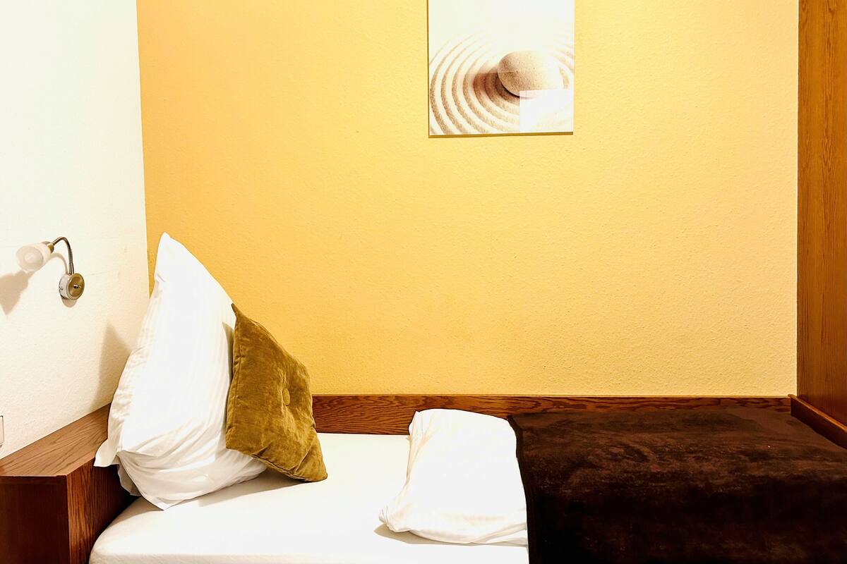 A hotel room with a bed, a nightstand, a wall-mounted picture, and a wooden headboard.