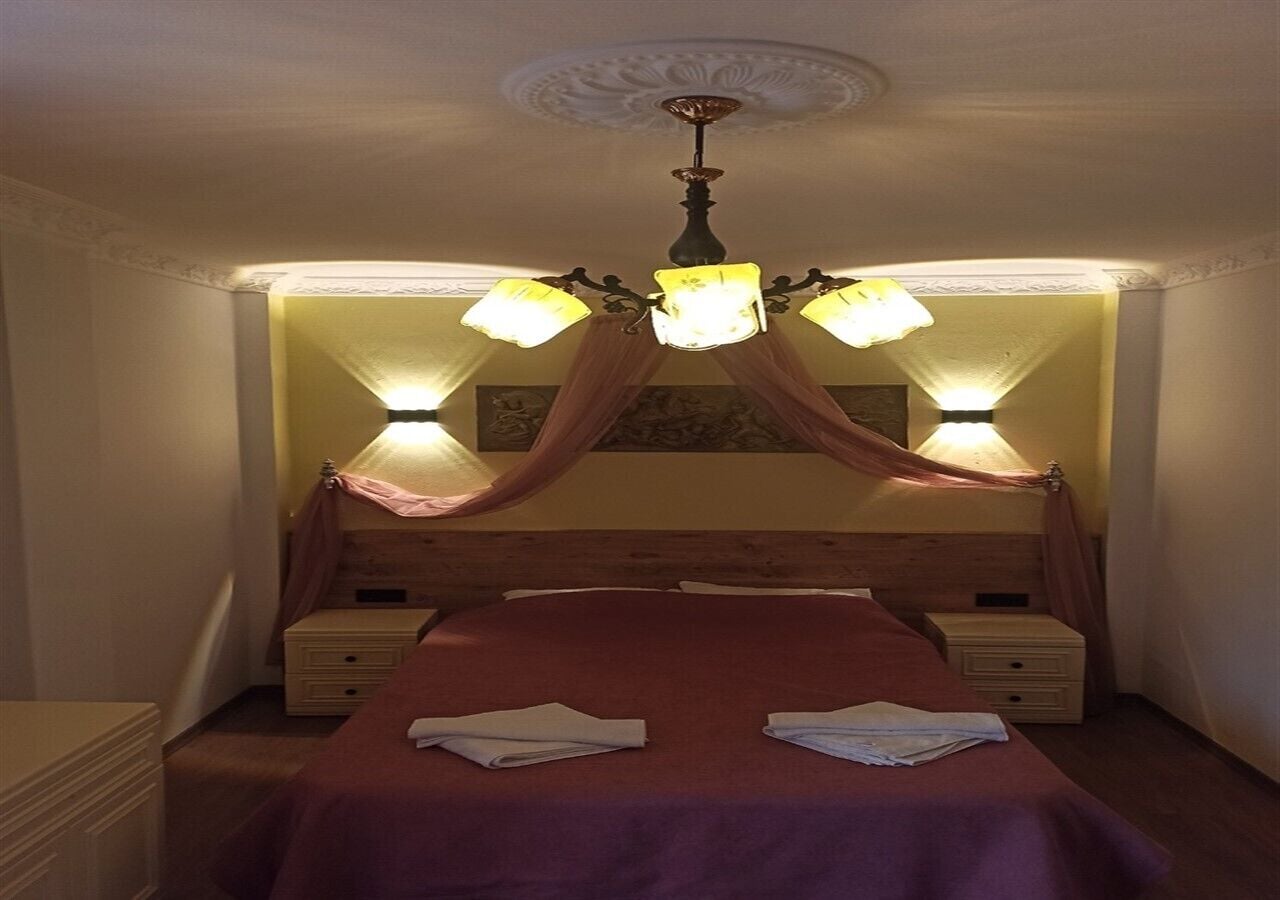 Un dormitorio con una cama con dosel, dos mesitas de noche y una araña.
