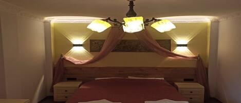 Un dormitorio con una cama con dosel, dos mesitas de noche y una araña.