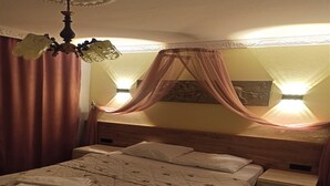 Un dormitorio con cama, mesitas de noche, dosel y candelabro.