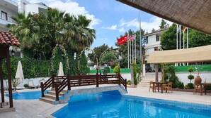 Una piscina con cubierta de madera, sillas de descanso y sombrillas.