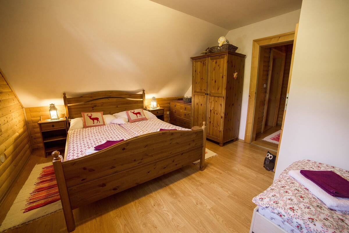 A wooden bed with a headboard, a nightstand with a lamp, a wooden wardrobe, and a small table with a lamp.