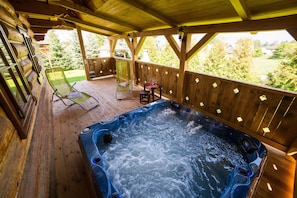 A wooden deck with a hot tub, two lounge chairs, and a table with a glass of wine. - Chalupky u babky (Liptovská Štiavnica)