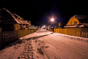 Calle nevada bordeada de casas de madera, iluminada por farolas.