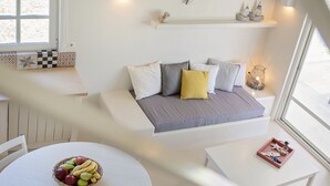 A modern, well-lit room with a round dining table, a sofa with cushions, and a window with a view. - Ta Spitakia (Kos)