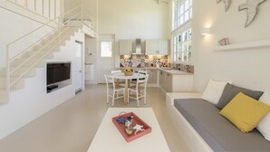 A modern interior with a staircase, a dining area, a kitchen, and a living room with a sofa and cushions. - Ta Spitakia (Kos)