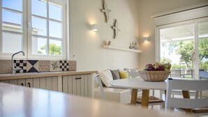 A kitchen with a white countertop, a dining table with chairs, and a basket of fruit on the table. - Ta Spitakia (Kos)