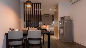 A compact hotel room with a dining area, a bed, a kitchenette, and an air conditioning unit. - VN HOUSE Beach (Da Nang)