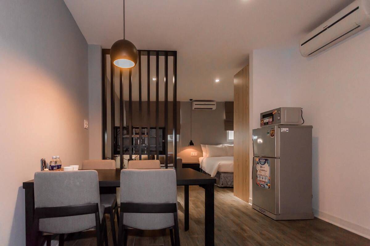 Una habitación de hotel compacta con zona de comedor, cama, kitchenette y aire acondicionado.