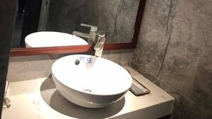 A bathroom with a round sink, a mirror, and a marble wall. - VN HOUSE Beach (Da Nang)