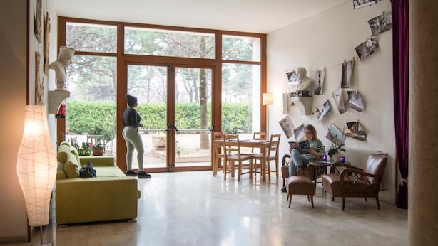 Un amplio salón con un ventanal grande, un sofá, una mesa de comedor y una persona leyendo.
