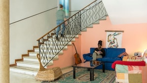 Una sala de estar con una escalera, un sofá azul, una mesa de centro y un cuadro de colores en la pared.
