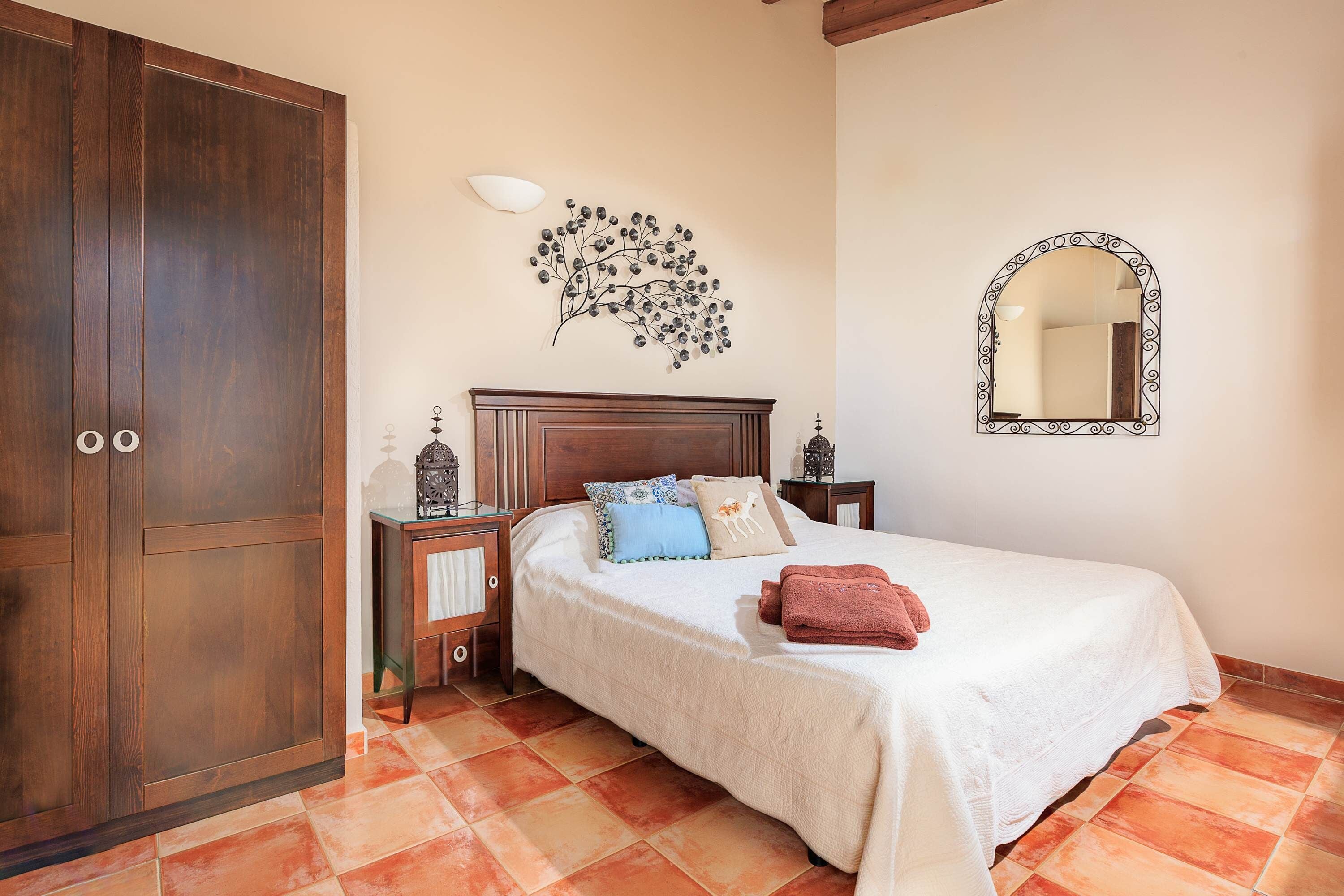 Un dormitorio con cama, armario, mesita de noche, espejo en la pared y un adorno mural.