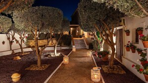 A courtyard with trees, potted plants, a stone pathway, and a staircase leading to an upper level.