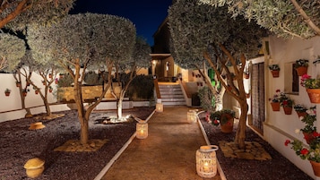 A courtyard with trees, potted plants, a stone pathway, and a staircase leading to an upper level.