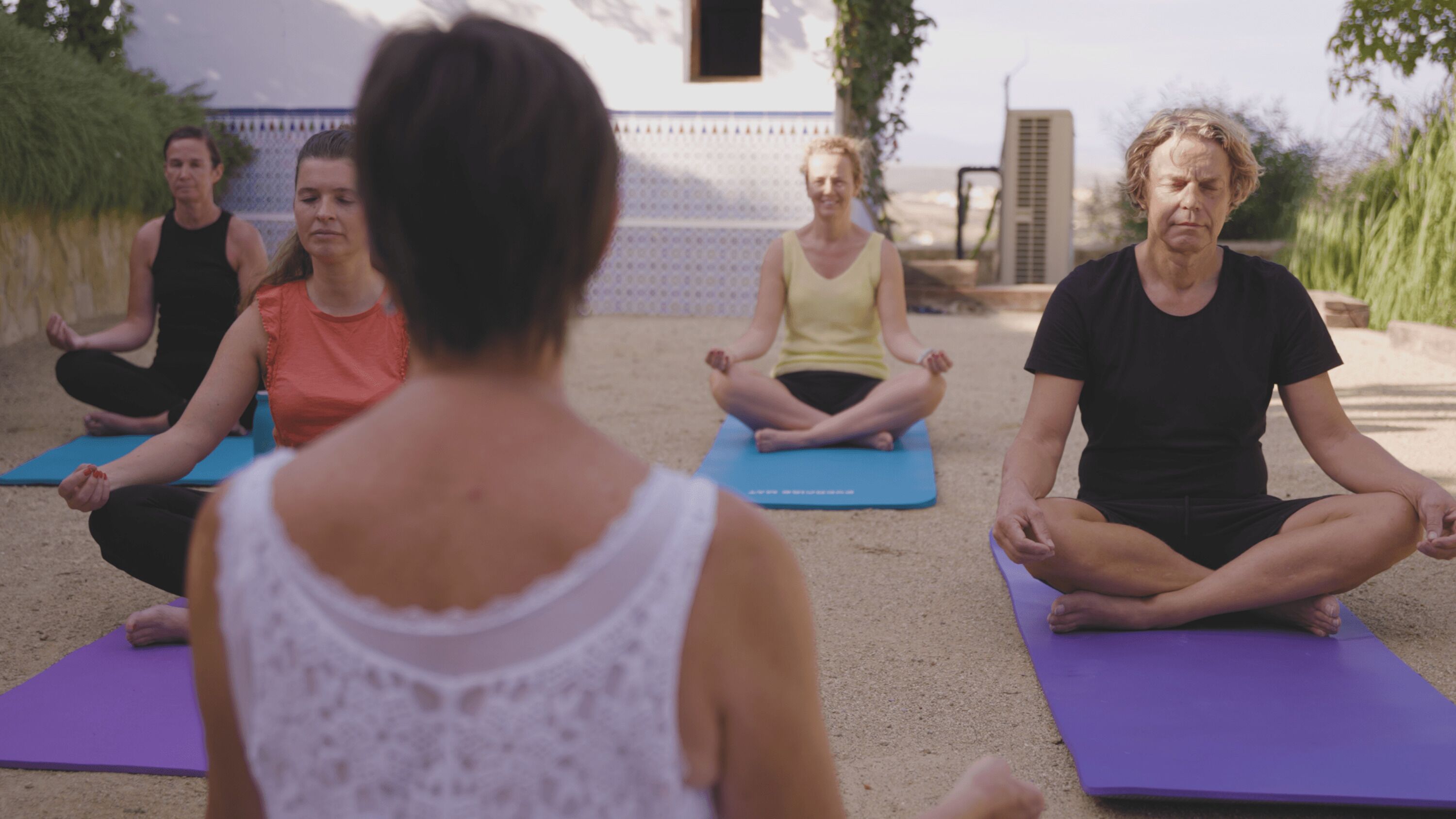 A group of people seated on yoga mats in an outdoor setting.