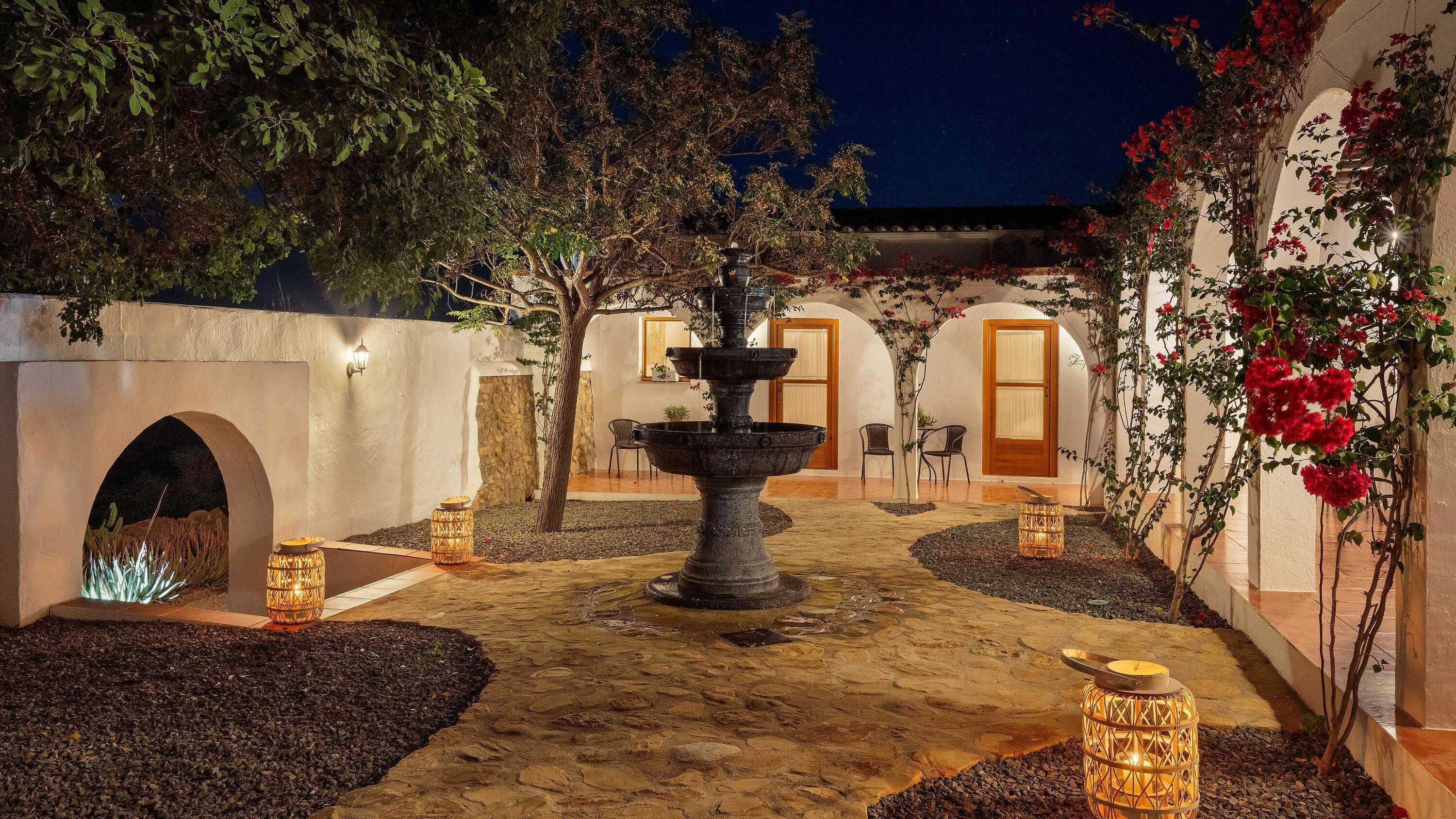 A courtyard with a central fountain, seating areas, and a building with arched doorways.