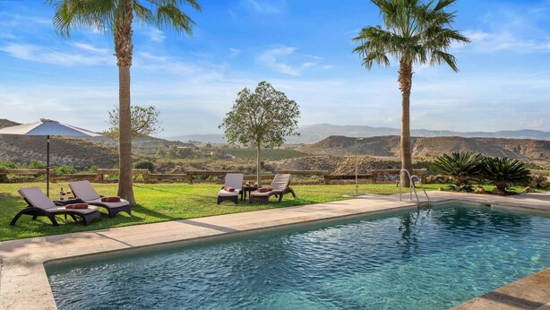 A pool area with lounge chairs, a table with a bottle, and a view of the landscape.