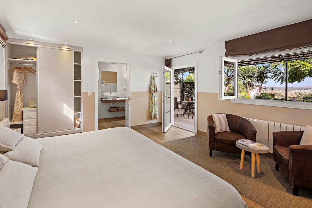 Quarto com cama grande, guarda-roupa, banheiro, área de estar e vista para o exterior.