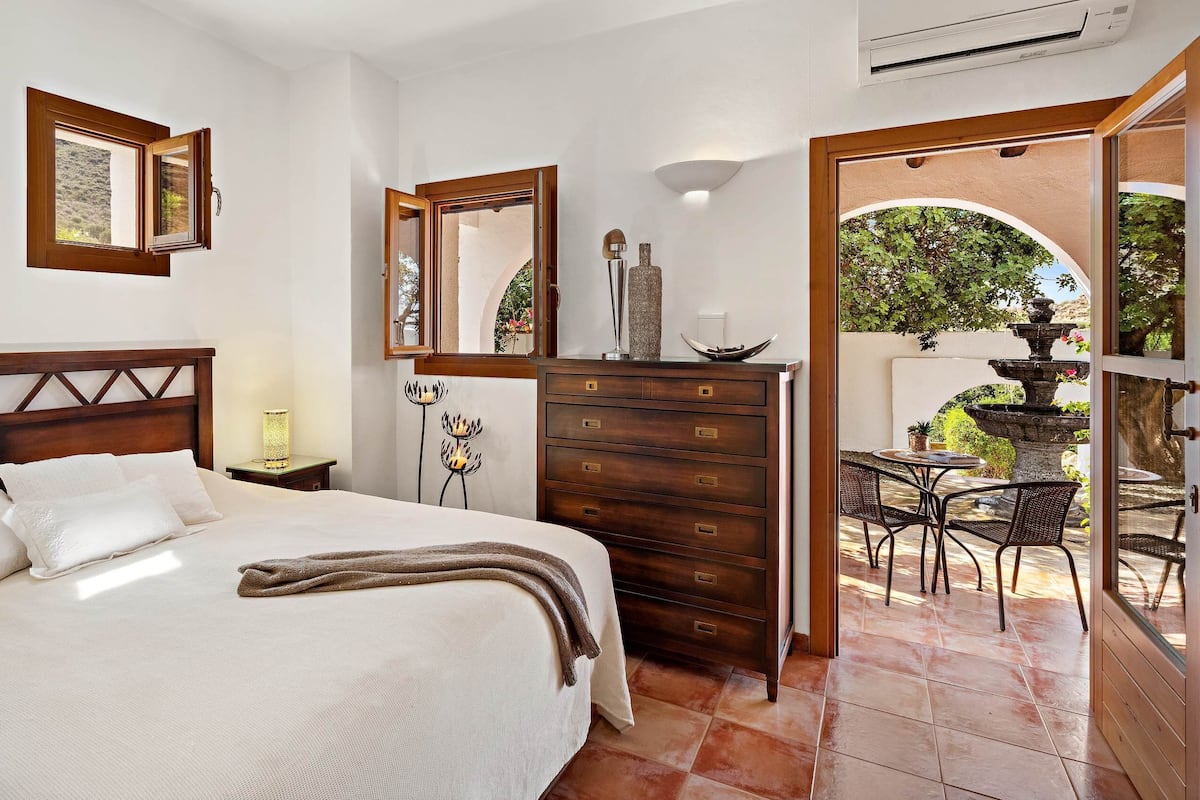 Quarto com cama, penteadeira e vista para um pátio externo.