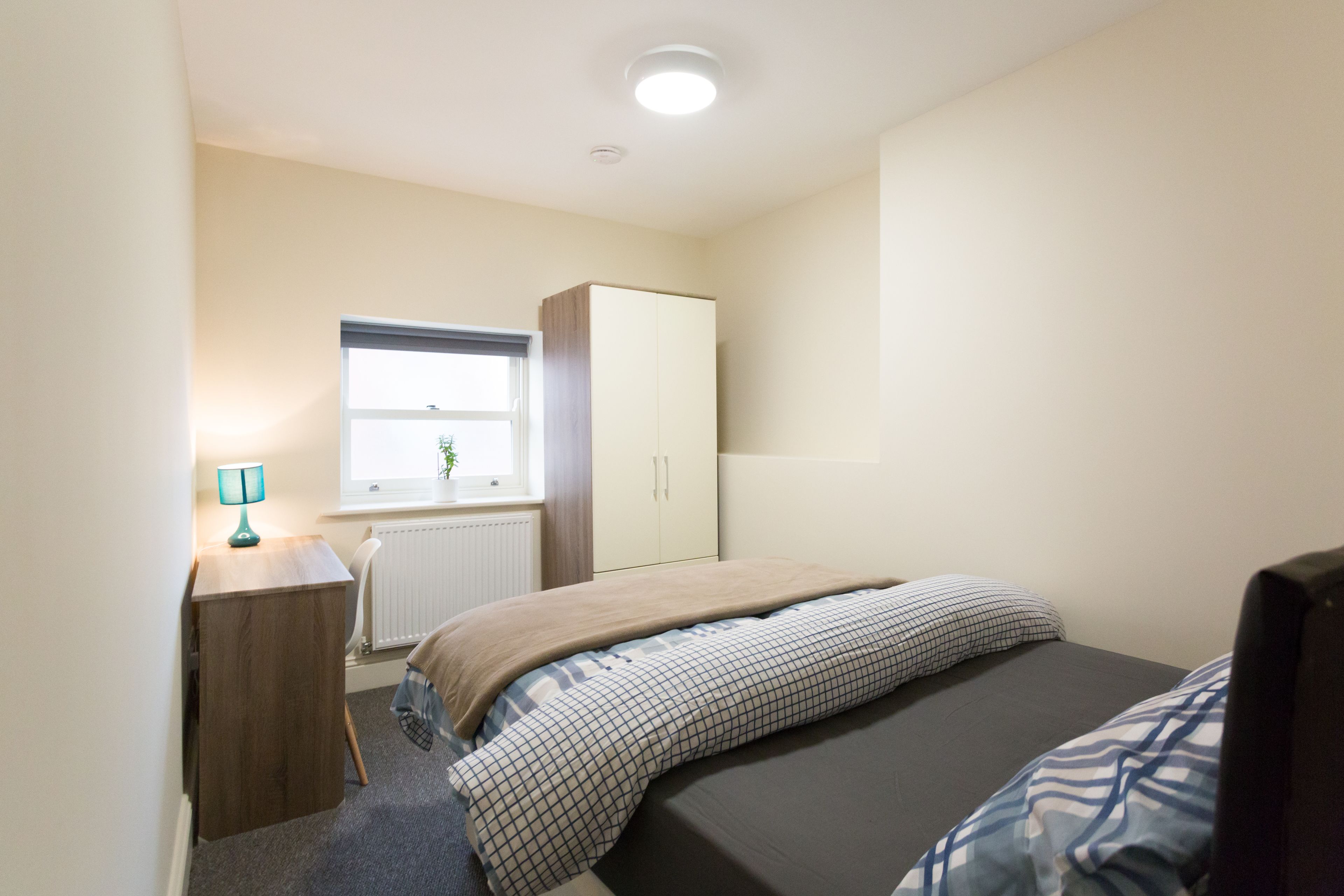 Une chambre à coucher avec un lit, une armoire, un bureau, une lampe et une fenêtre.