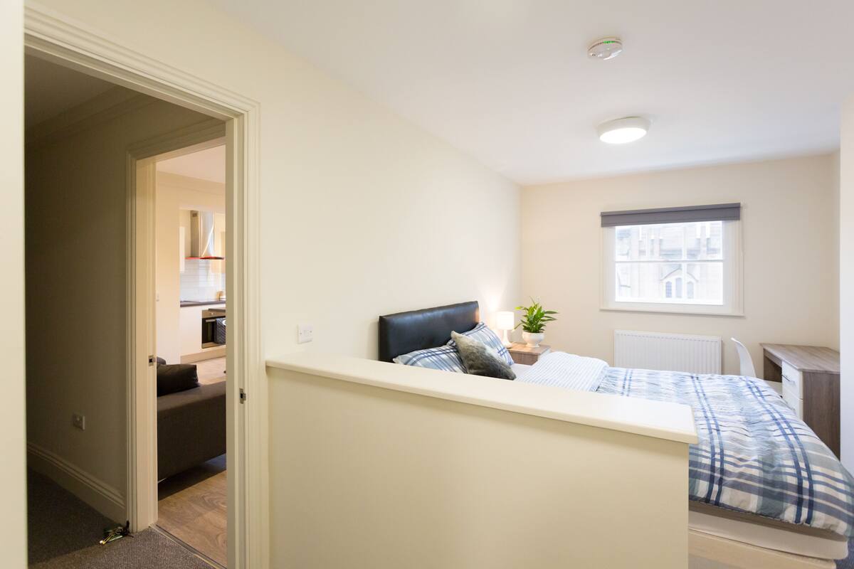 A bedroom with a bed, bedside table, lamp, and window.