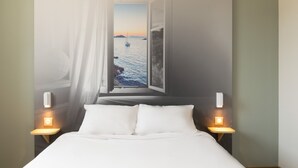 A bedroom with a bed, two bedside tables with lamps, and a large window with a view of the sea and a sailboat. - B&B HOTEL MARSEILLE La Valentine Saint-Menet (Marseille)