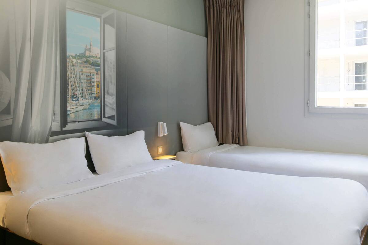 A hotel room with two beds, a large window with a view of a cityscape, and a painting on the wall.