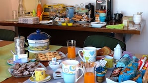 A breakfast table with various food items, a coffee maker, and a painting on the wall.