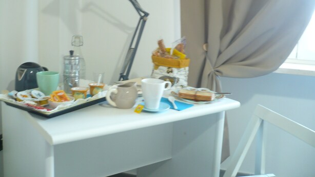A desk with a lamp, a coffee maker, a mug, a plate with food, and a basket of bread.