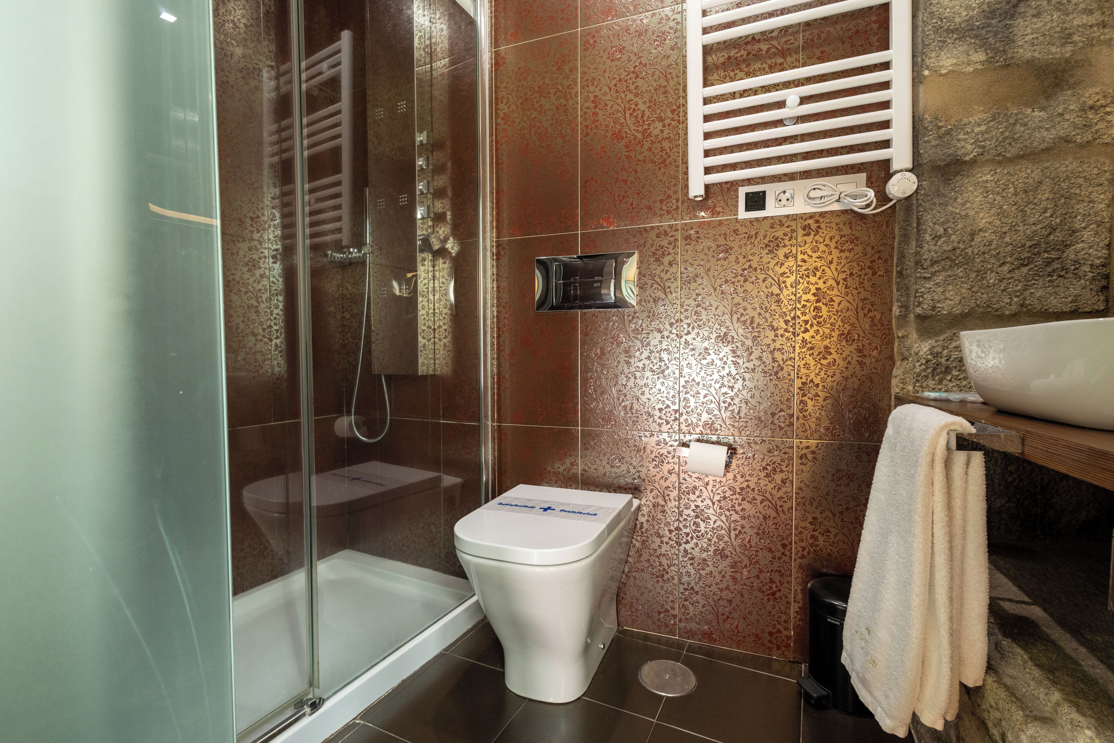 A bathroom with a glass-enclosed shower, a toilet, and a sink with a towel rack.