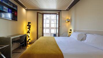 A hotel room with a bed, a desk, a chair, a standing lamp, and a television mounted on the wall.