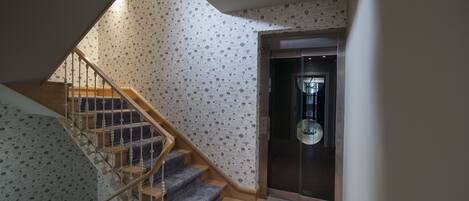 Una escalera con papel tapiz estampado y una puerta de ascensor de vidrio.