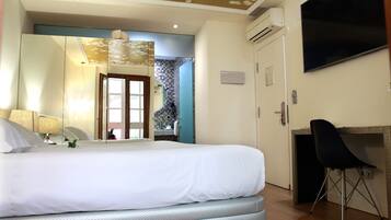 A hotel room with a large bed, a desk with a chair, a TV, and a bathroom visible through an open door.