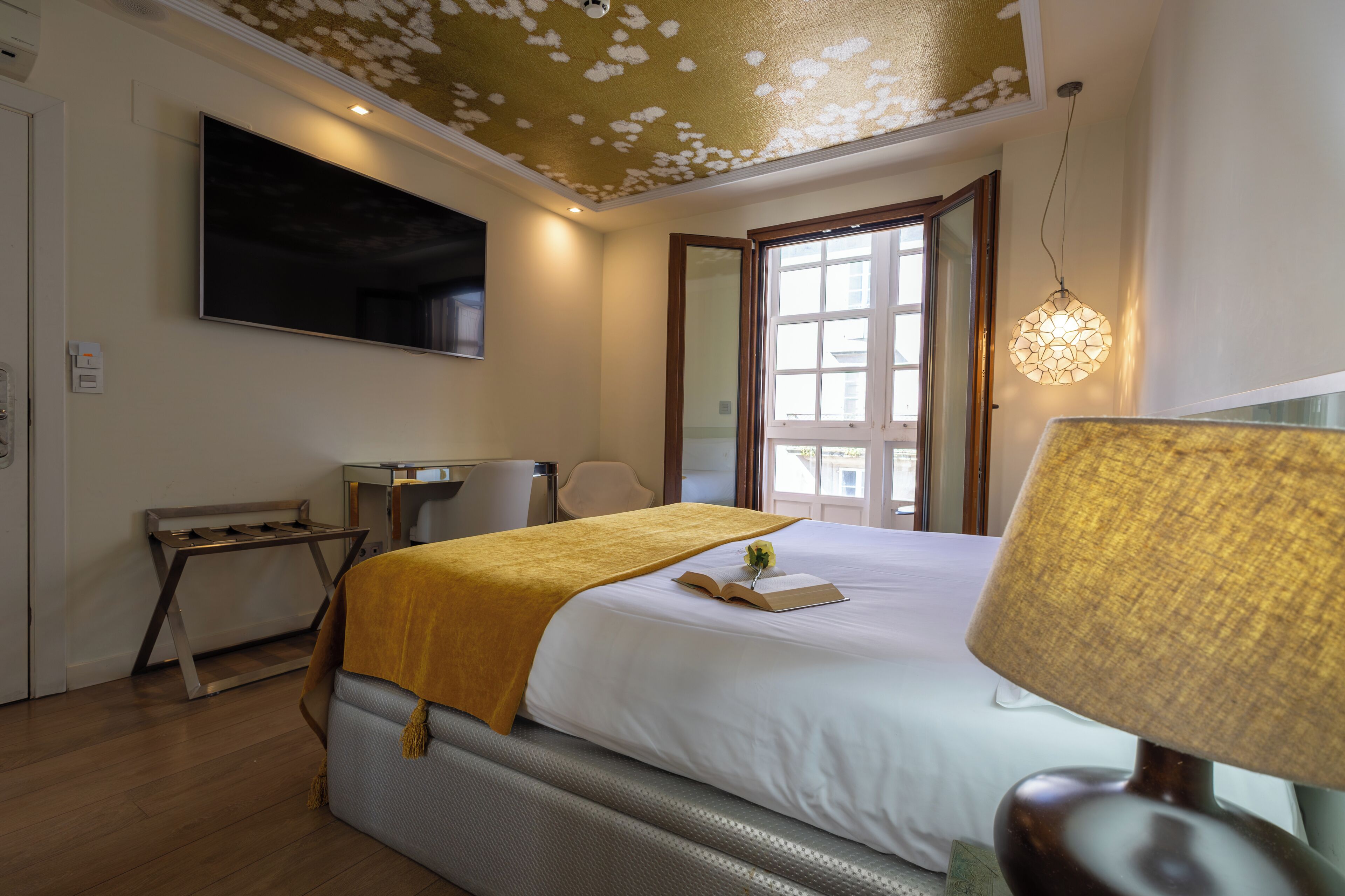 Une chambre d’hôtel avec un lit, un bureau, une chaise, une lampe et une grande fenêtre.