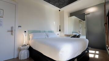 Una habitación de hotel moderna con cama, mesita de noche y espejo.