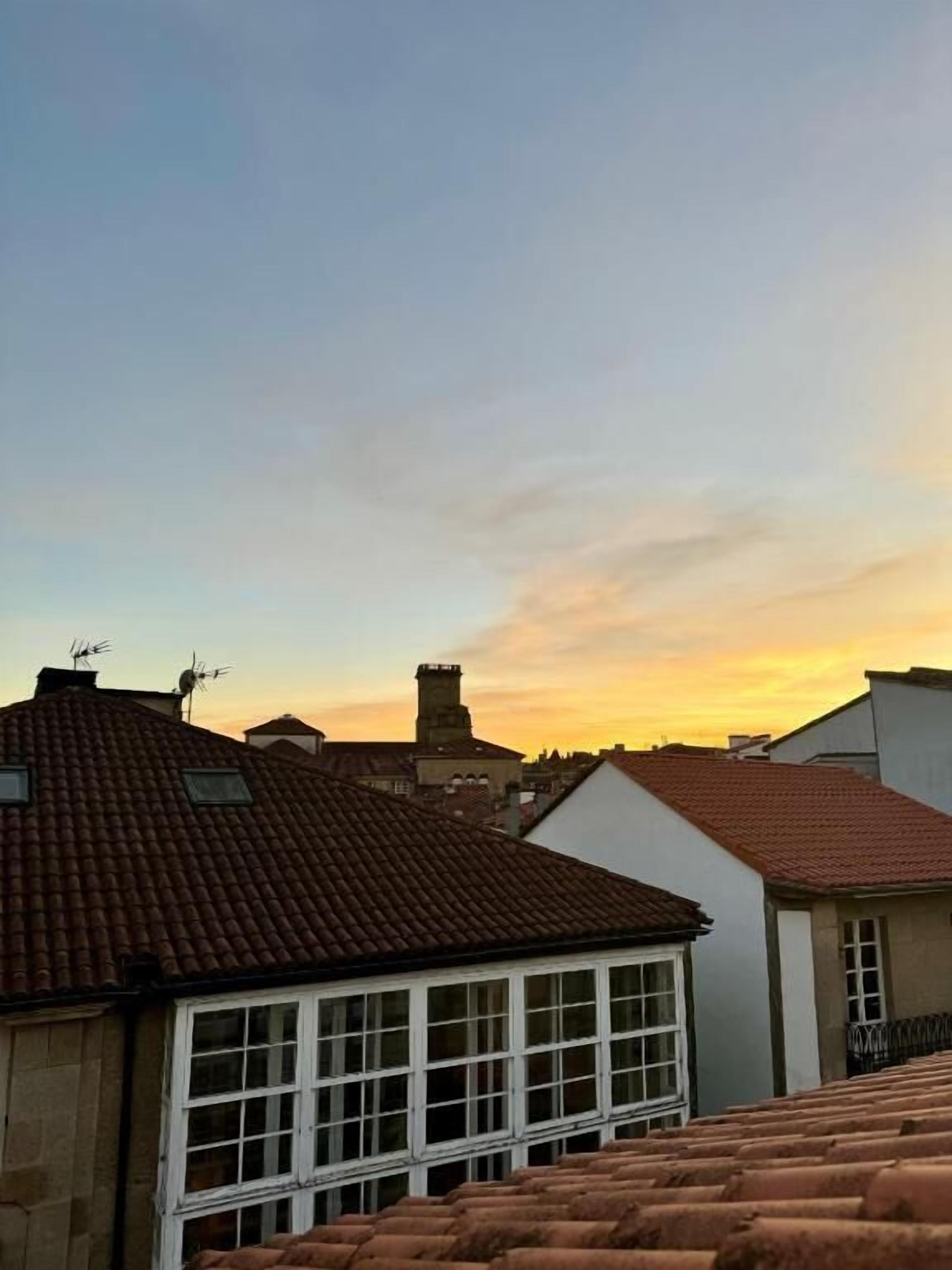 A residential area with terracotta-tiled roofs, white window frames, and a clear sky at sunset.